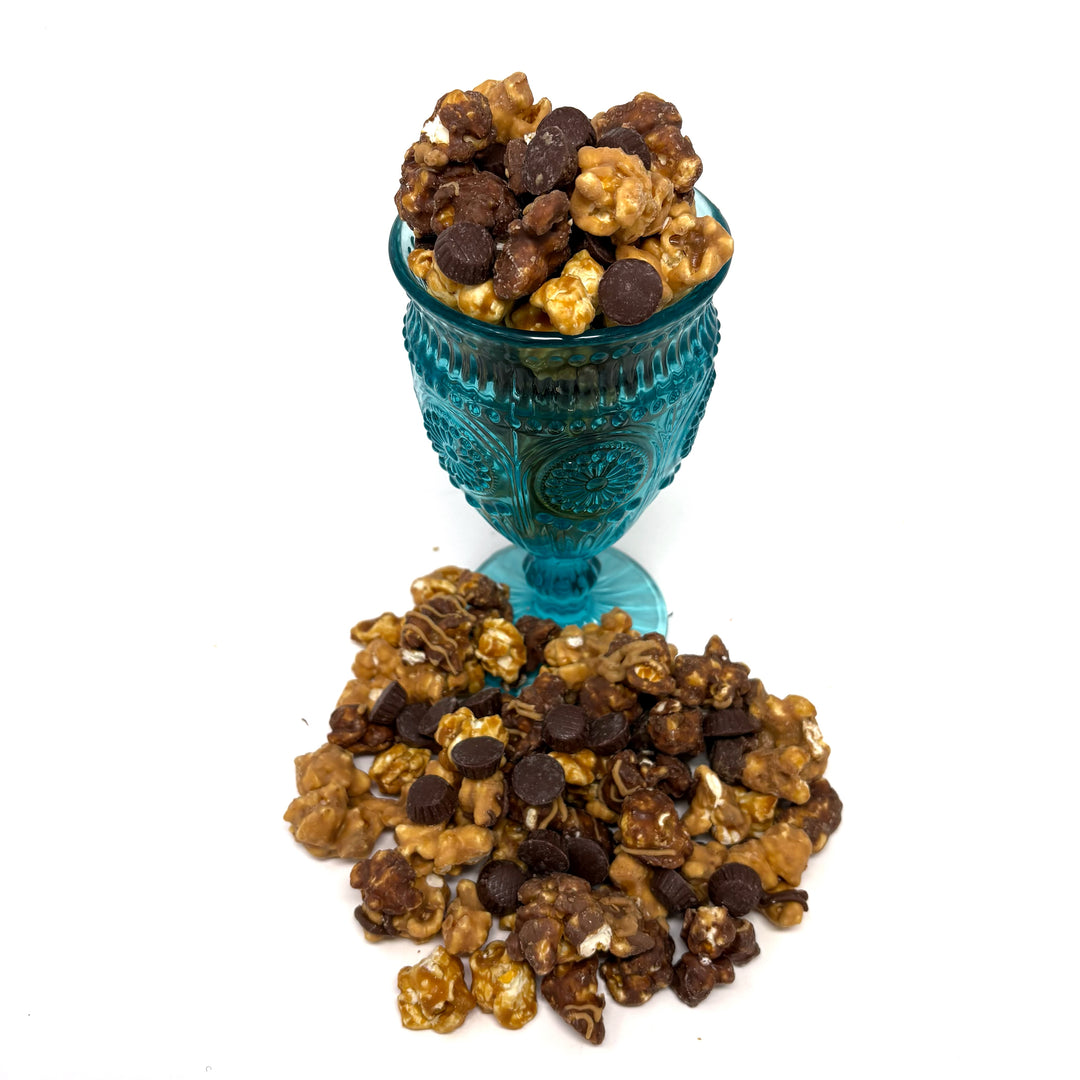 A close up of our Ultimate Peanut Butter Cup Popcorn with our creamy peanut butter caramel popcorn and chocolate caramel popcorn that is topped with yummy mini peanut butter cups.